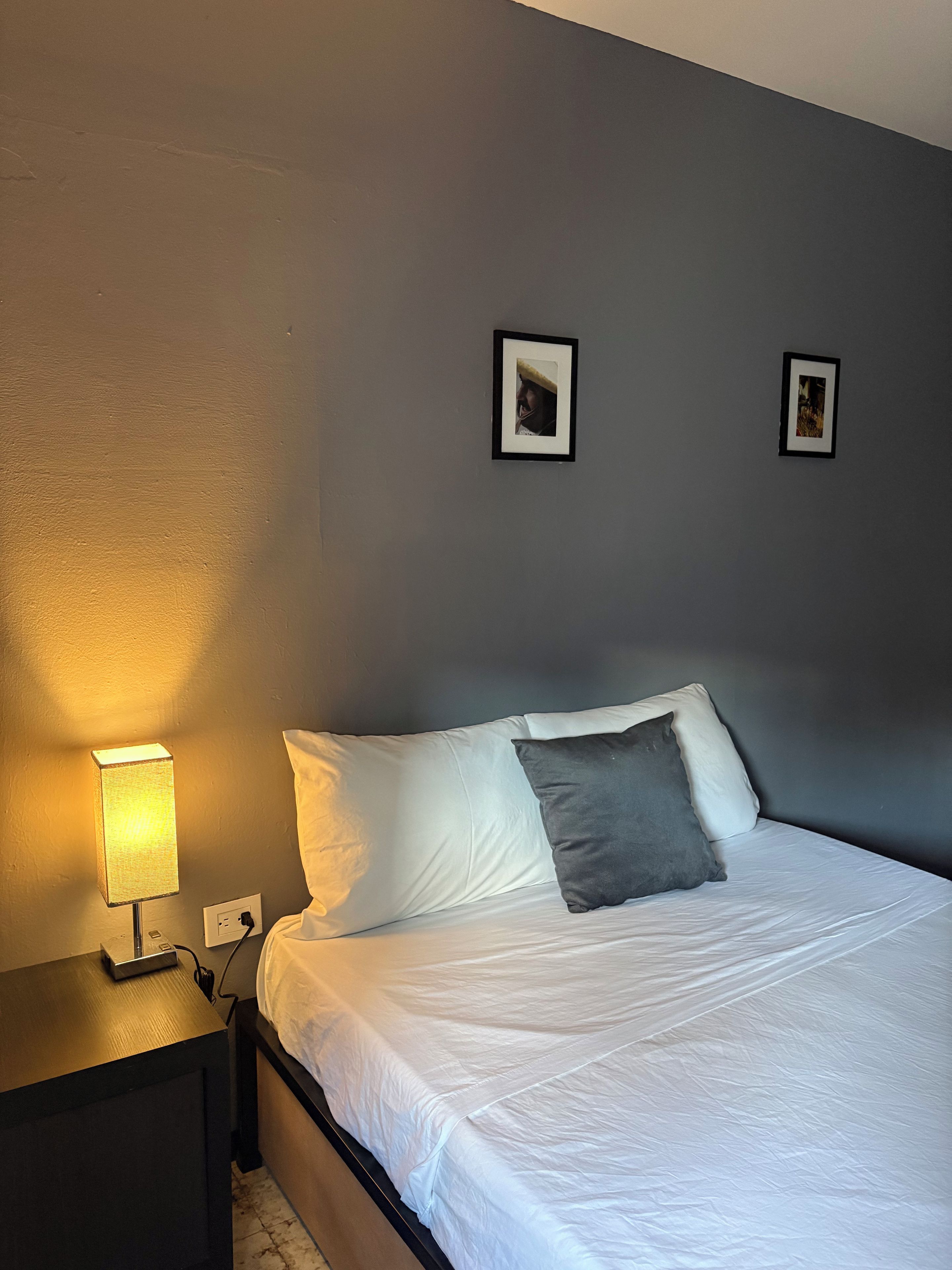 A bedroom with a bed, a nightstand, a lamp, and two framed pictures on the wall.