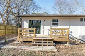 Une maison de plain-pied dotée d’un porche à l’avant, d’une porte-fenêtre coulissante et d’un petit espace extérieur aménagé avec deux bancs en bois.
