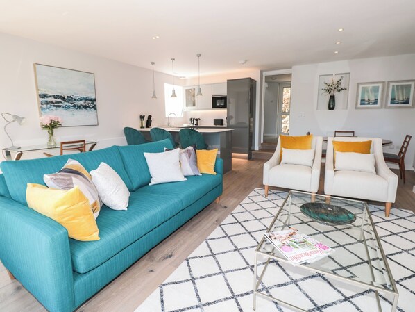 A modern living room with a teal sofa, white armchairs, and a glass coffee table. - Galvayne (Dartmouth)