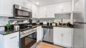 A modern kitchen with white cabinets, stainless steel appliances, and a marble backsplash. - Cozy Creekside Landing (Branson)