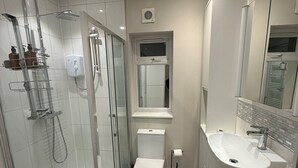 Ett modernt badrum med en dusch som är avskärmad med glasväggar, en vit toalett och ett handfat med en spegel ovanför.