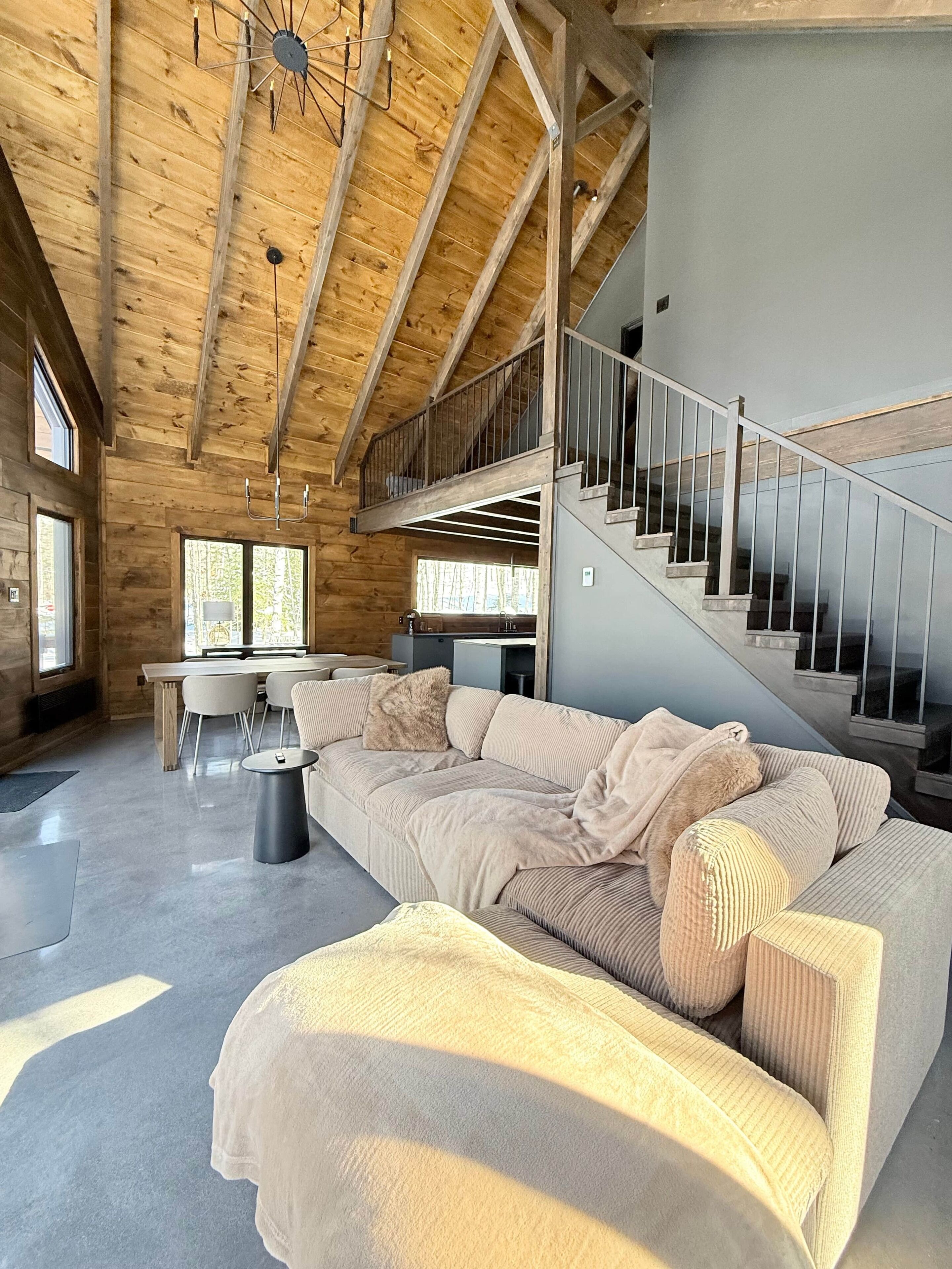A spacious living area with a large sectional sofa, a dining table, and chairs. A staircase with a metal railing leads to an upper level.