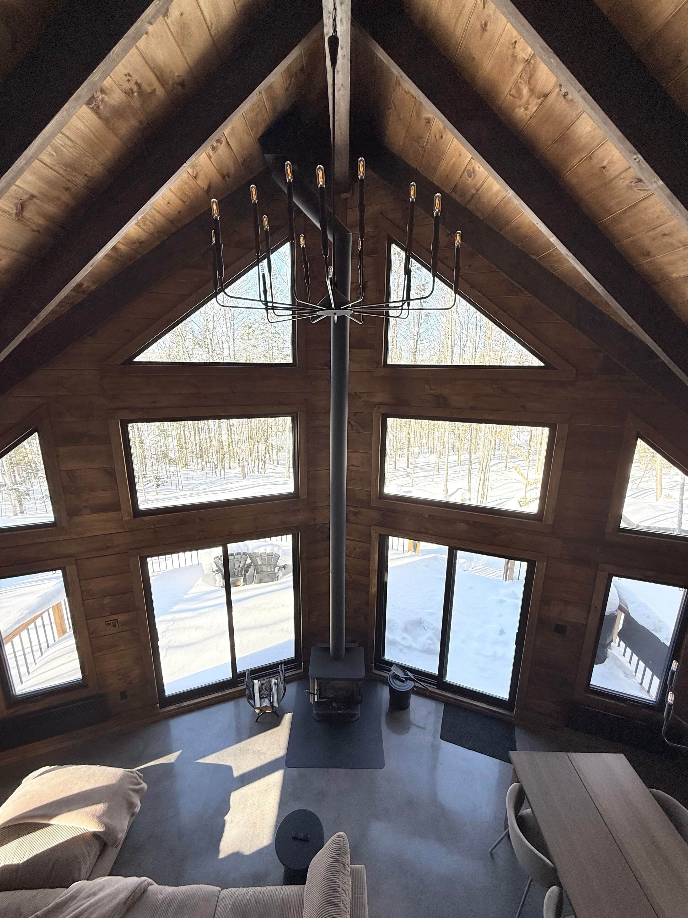 Una cabaña de madera con techos altos, una chimenea central, ventanas amplias y una zona de estar acogedora.