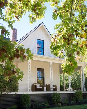 A two-story house with a white exterior, a visible chimney, and a covered porch with two chairs. - Kubli Haus (Jacksonville)