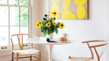 A room with a round white table, two wooden chairs, a vase with sunflowers, and a yellow abstract painting on the wall.