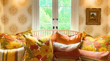 A cozy room with a white bench, floral cushions, and a window with a view of greenery.
