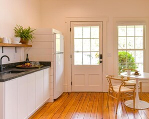 A kitchen with white cabinets, a wooden countertop, a sink, a refrigerator, and a dining area with a table and chairs.