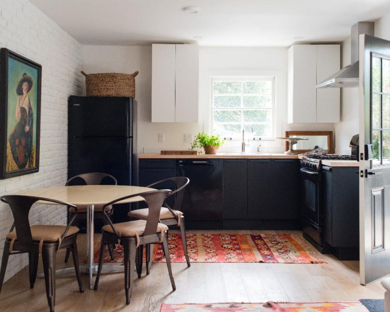 Cocina moderna con refrigerador negro, armarios blancos, ventana y comedor con sillas y mesa.