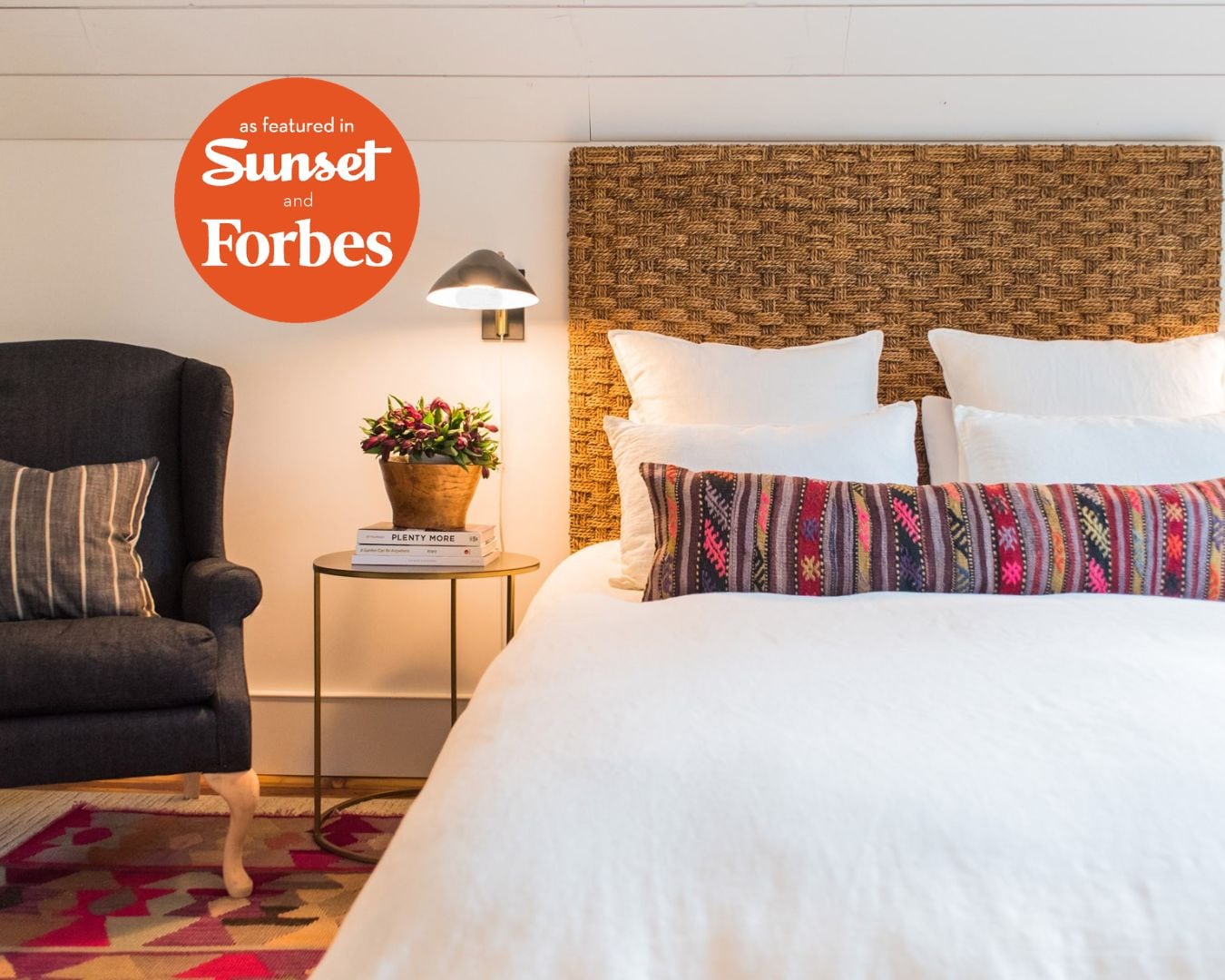 Habitación de hotel con cama, una silla, una mesita de noche con lámpara, y un aplique de pared.