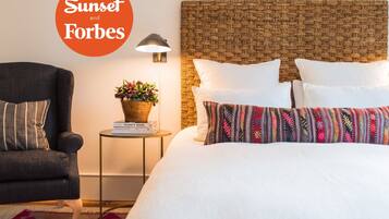 A hotel room with a bed, a chair, a side table with a lamp, and a wall-mounted light fixture.