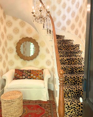 A staircase with a leopard print carpet, a white sofa with patterned cushions, a round mirror, and a chandelier. - Kubli Haus (Jacksonville)