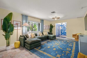Una sala de estar con un sofá modular, una alfombra estampada y plantas grandes.