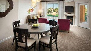 Een hotelkamer met een eettafel, stoelen, een bank, een televisie en een open haard.