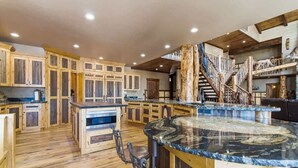 Una cocina amplia con armarios de madera, una isla central con encimera de mármol y una escalera rústica.