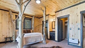 Un dormitorio con cama, ramas de abedul, alfombra de piel y techo de madera.