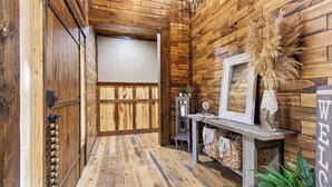 Un pasillo interior de madera con un diseño rústico, que incluye una puerta de madera, un espejo enmarcado y un letrero de bienvenida.