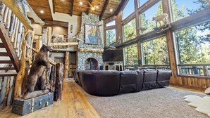 Un interior rústico con chimenea de piedra, vigas de madera y un amplio ventanal con vistas al exterior.