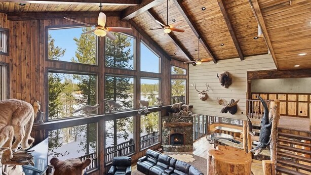 Un salón amplio con chimenea, sofás de cuero y ventanas grandes que ofrecen vistas al exterior.