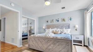 Une chambre à coucher comprenant un lit, des tables de chevet, un ventilateur de plafond et des œuvres d’art murales.
