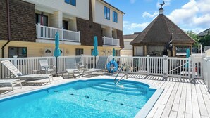 Une piscine avec des chaises longues et des parasols, un belvédère couvert et une clôture blanche.