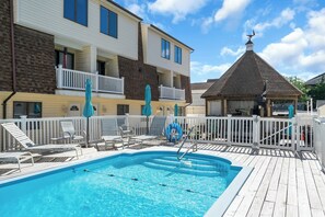 A swimming pool with lounge chairs and umbrellas, a covered gazebo, and a white fence. - Professionally Managed | Walk to Beach (Seaside Heights)
