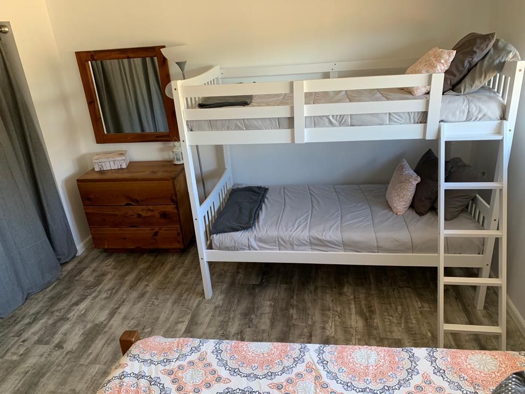 Een stapelbed met een ladder, een houten dressoir, een spiegel en een bedspread met dessin.