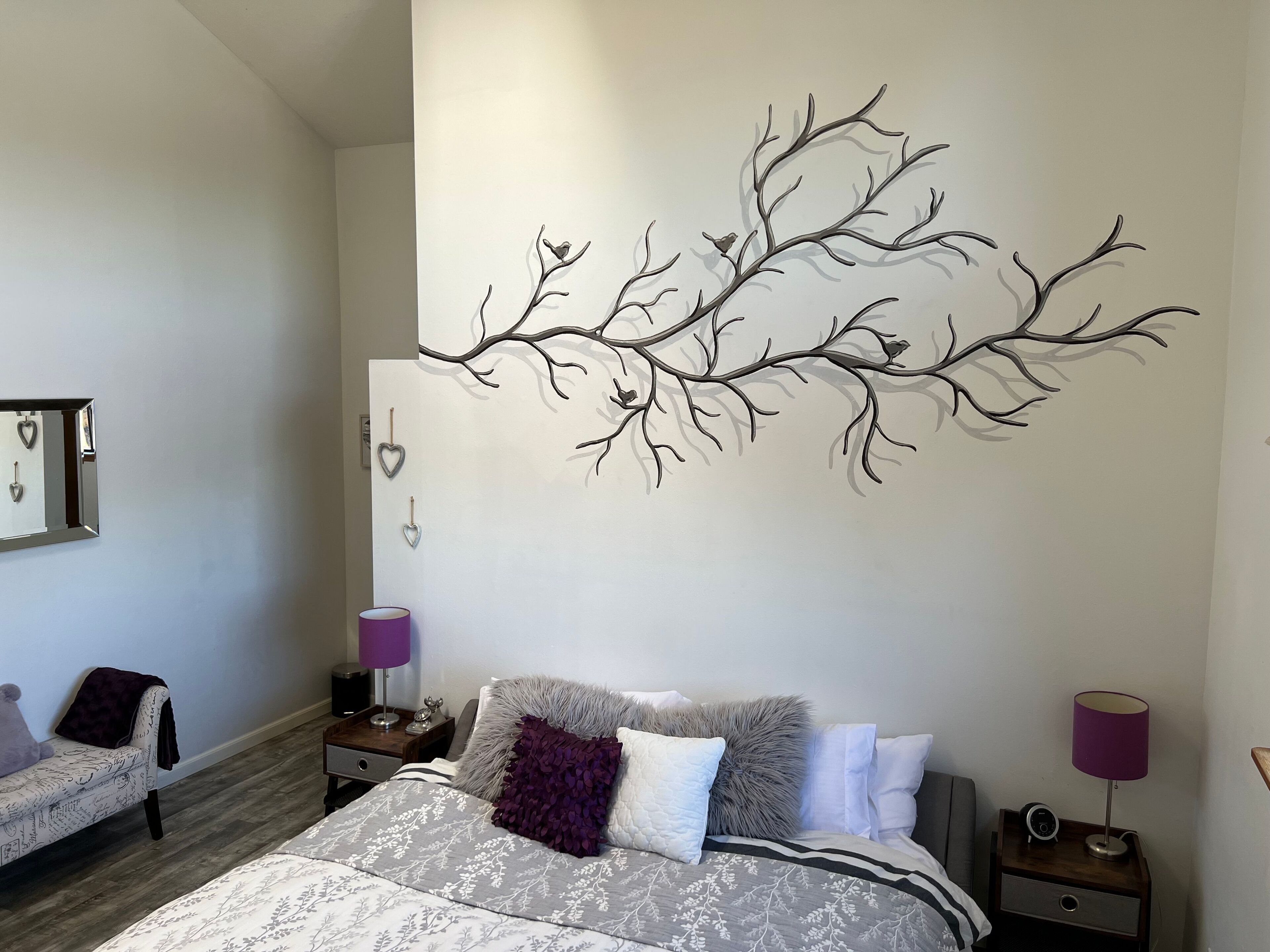 Un dormitori amb un llit gran, dues taules de nit amb làmpades, una cadira i una decoració de branca d'arbre penjada a la paret.