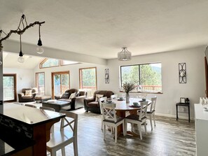 A spacious living area with a dining table, multiple seating options, and large windows offering natural light and views of the outdoors. - Ski Chalet - Views, Hot Tub, Game Room (Angel Fire)