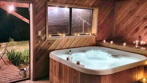 A wooden interior with a hot tub, a window with lights, and a view of the outdoors. - Ski Chalet - Views, Hot Tub, Game Room (Angel Fire)