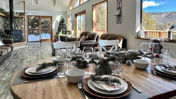 A spacious living area with a high ceiling, a fireplace, and a view of a snowy landscape through large windows. - Ski Chalet - Views, Hot Tub, Game Room (Angel Fire)