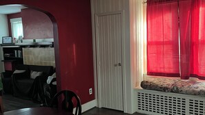 Ein Essbereich mit Holztisch und Stühlen, einem Deckenventilator, einem Fenster mit roten Vorhängen und einer Tür mit weißem Vorhang.