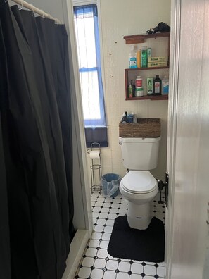 A bathroom with a toilet, a shelf with toiletries, a window with a curtain, and a trash bin. - Two bedroomhome to rent Thursday through Sunday morning for NFL draft (Pittsburgh)