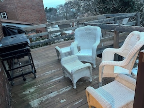 Een houten terras met wickerstoelen en een barbecue.