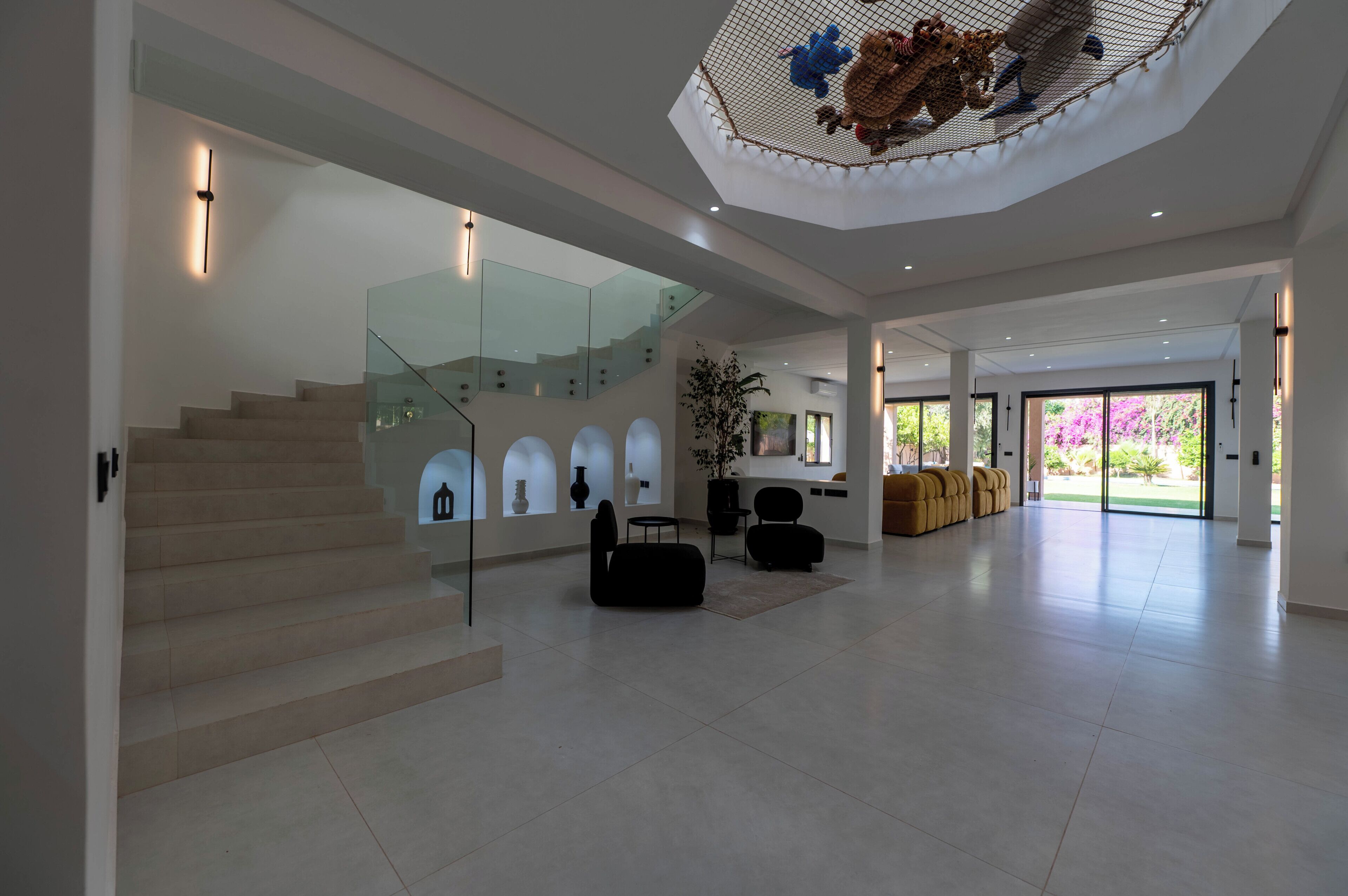 A spacious interior with a staircase, a glass railing, a large window, and a ceiling with a decorative element.