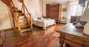 A bedroom with a wooden ladder, a bed with a white bedspread, a wooden wardrobe, and a desk with a lamp.