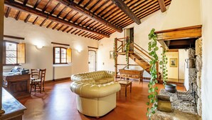A spacious living room with a leather sofa, wooden staircase, and a stone wall with pots. - Locanda Casalta (Strove)