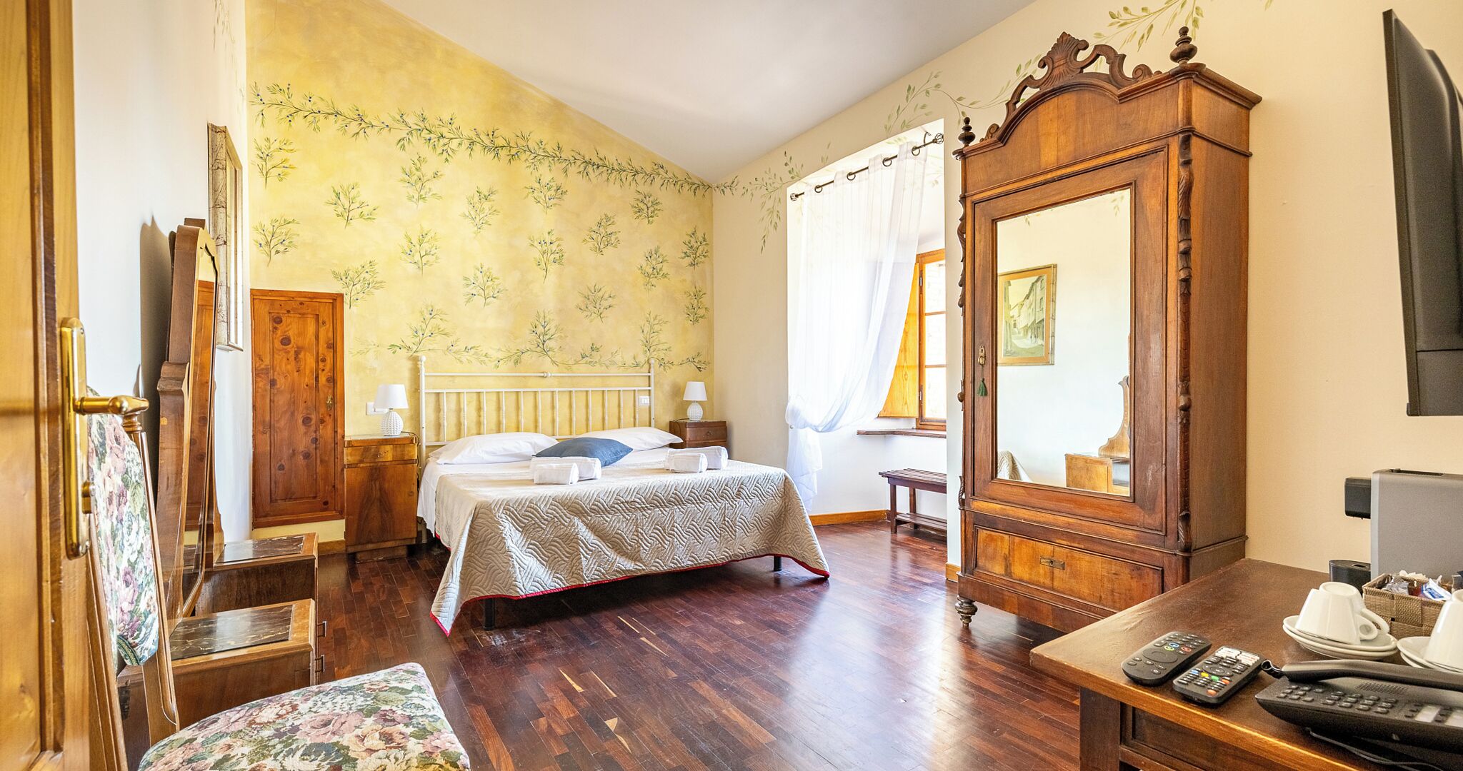 Une chambre à coucher avec un lit en bois, un grand miroir, une commode en bois, un bureau avec un téléphone et une chaise.