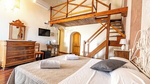 A bedroom with a wooden staircase, a dresser, a television, and a bed with pillows. - Locanda Casalta (Strove)