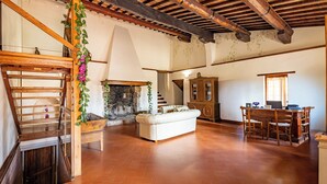 A spacious living area with a fireplace, a staircase, a dining area with a wooden table and chairs, and a sofa. - Locanda Casalta (Strove)