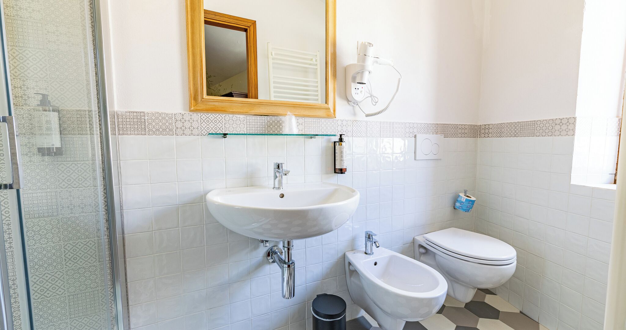 Un baño con lavamanos blanco, un bidé, inodoro y cabina de ducha de vidrio, además de un espejo.