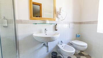 Un baño con lavamanos blanco, un bidé, inodoro y cabina de ducha de vidrio, además de un espejo.