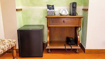 Une chambre de taille modeste, équipée d’un petit bureau en bois, d’un réfrigérateur, d’un téléphone et d’une machine à café.