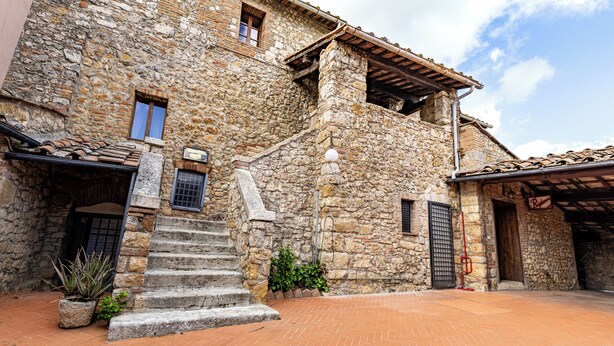 A stone building with a staircase leading to a second floor, a small garden area, and a red brick courtyard. - Locanda Casalta (Strove)