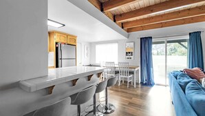 A modern kitchen with a central island, white bar stools, and a dining area with white chairs. - Bear Mesa Chalet | Hot Tub · Fireplace (Big Bear)