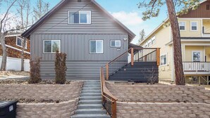 A two-story house with a grey exterior, a front porch, and a staircase leading to the entrance. - Bear Mesa Chalet | Hot Tub · Fireplace (Big Bear)