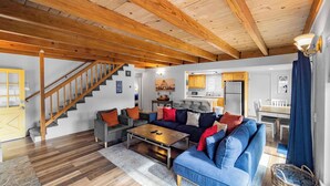 A spacious living area with a wooden staircase, a blue sofa set, and a kitchen area in the background. - Bear Mesa Chalet | Hot Tub · Fireplace (Big Bear)
