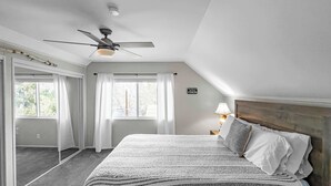 A bedroom with a large bed, a ceiling fan, a window with curtains, and a sign on the wall. - Bear Mesa Chalet | Hot Tub · Fireplace (Big Bear)