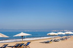 A beach with rows of sun loungers and umbrellas, a clear sky, and a calm sea. - Luxury Vidanta Resort Escape - Pools, Lazy River Beach Access, family-friendly (Q.R.)