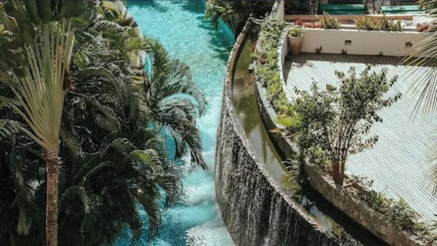 A pool with a waterfall feature, surrounded by tropical vegetation and a stone wall. - Luxury Vidanta Resort Escape - Pools, Lazy River Beach Access, family-friendly (Q.R.)