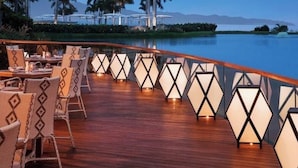 A deck with outdoor seating and a view of palm trees and a distant mountain range. - Luxury Vidanta Resort Escape - Pools, Lazy River Beach Access, family-friendly (Q.R.)